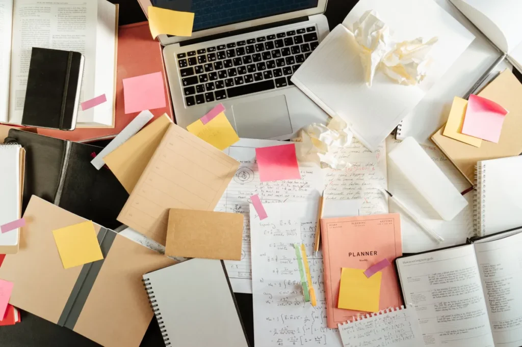 Cluttered desk with a laptop, notebooks and sticky notes